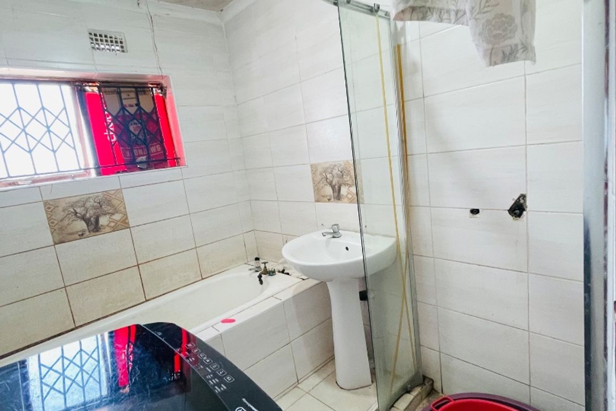 A bathroom featuring a pedestal basin, built-in bathtub, and glass shower enclosure, currently requiring maintenance and repairs to ceiling and fixtures.