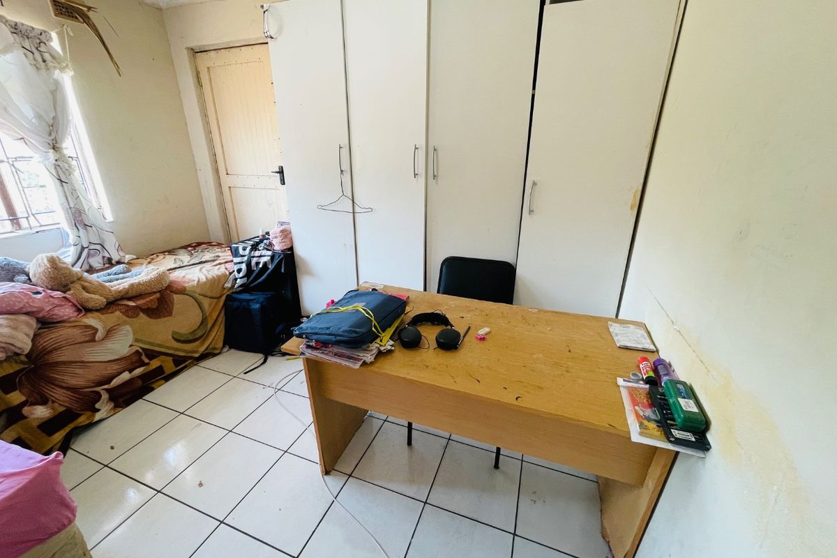 A bedroom featuring tiled flooring and built-in cupboards, currently showing signs of wear including wall staining and ceiling damage.