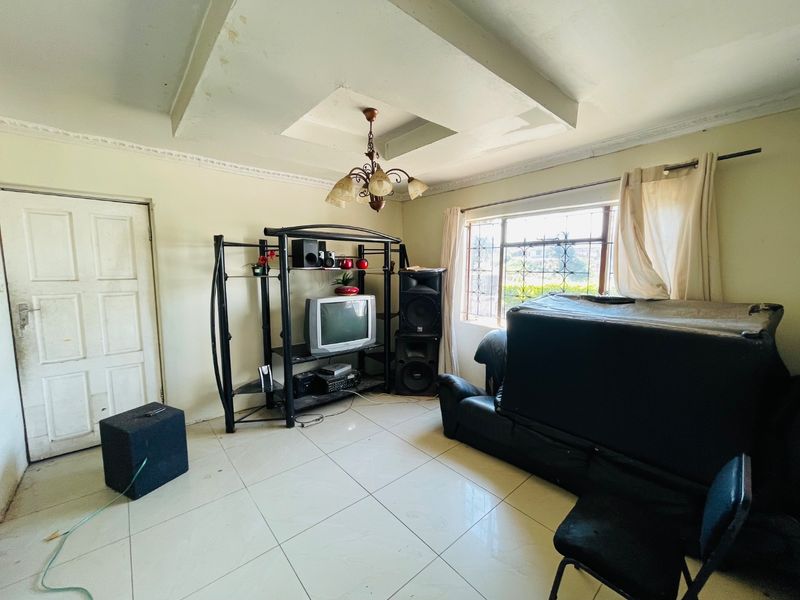 A living room featuring tiled flooring, a recessed ceiling detail, and security bars on the window, requiring cosmetic updates to improve its overall condition.