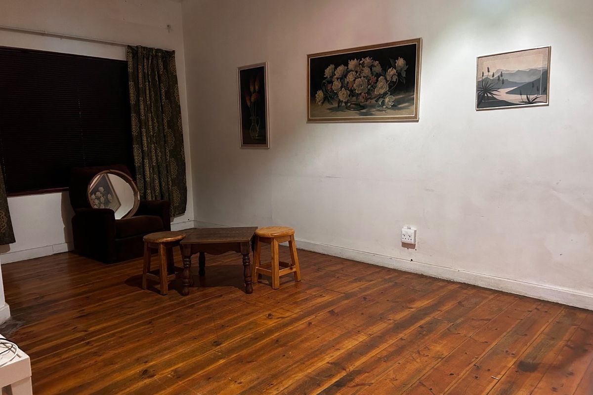 A living room featuring original hardwood flooring, white walls, and a ceiling vent, offering a blank canvas for potential interior design updates.