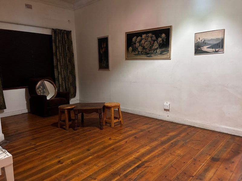 A living room featuring original hardwood flooring, white walls, and a ceiling vent, offering a blank canvas for potential interior design updates.