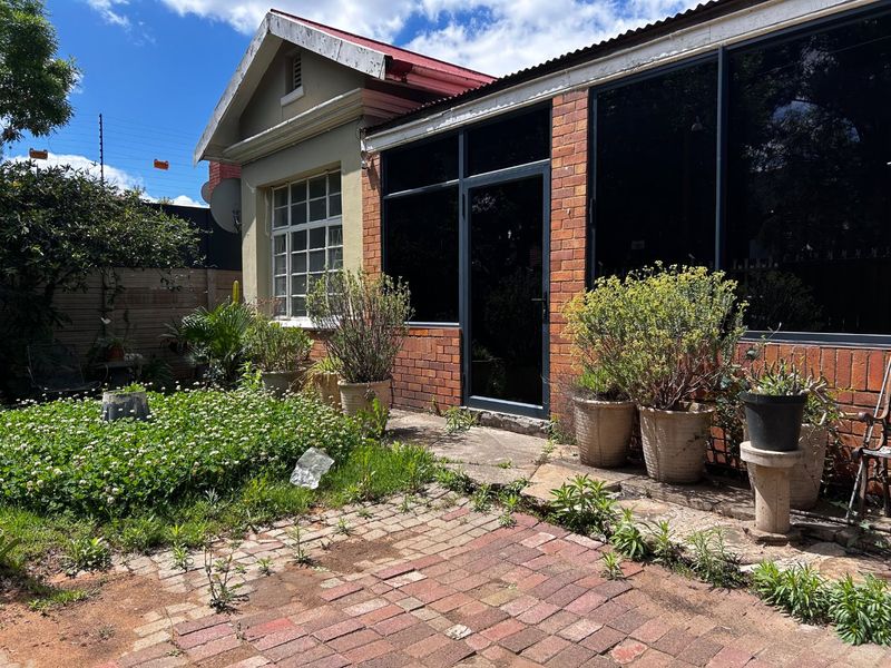 Rear exterior view of the house featuring a brick facade, paved patio area, and aluminium framed windows with a metal roof.