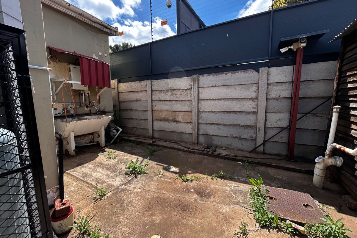 A rear utility courtyard featuring a concrete sink, security fencing, and paved flooring, requiring maintenance and landscaping to improve the outdoor space.