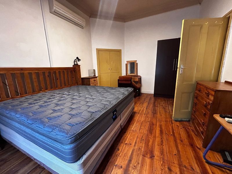 A bedroom featuring original hardwood flooring, a built-in cupboard, and a wall-mounted air conditioning unit.