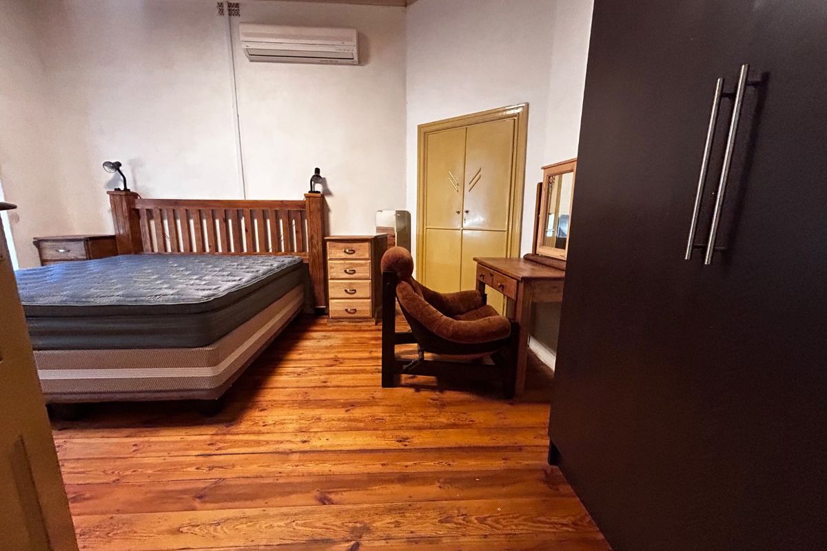 Spacious bedroom featuring original hardwood flooring, a wall-mounted air conditioning unit, and built-in storage cabinetry.