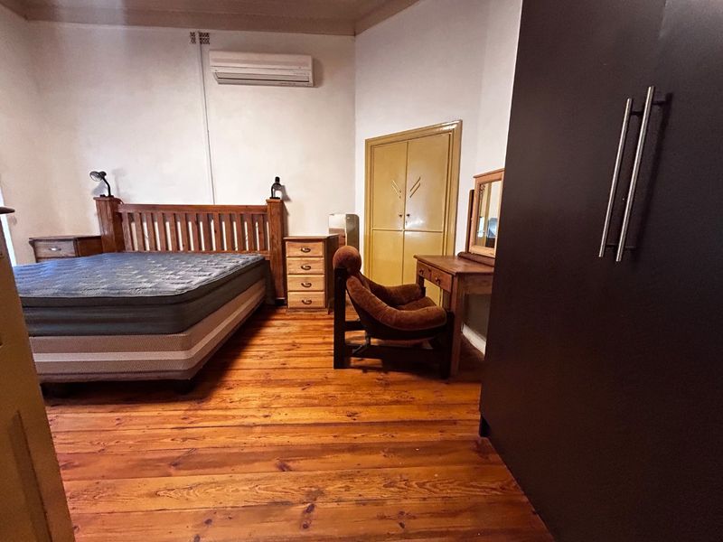 Spacious bedroom featuring original hardwood flooring, a wall-mounted air conditioning unit, and built-in storage cabinetry.