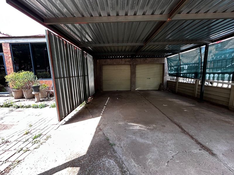 A covered carport area featuring a corrugated metal roof, concrete flooring, and dual roller garage doors, providing sheltered parking space.
