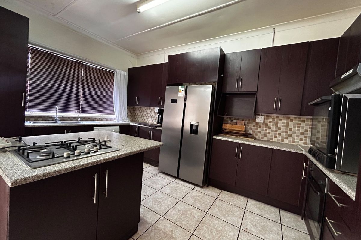 A functional kitchen featuring dark wood cabinetry, granite countertops, a gas hob, built-in oven, and tiled flooring with a mosaic backsplash.