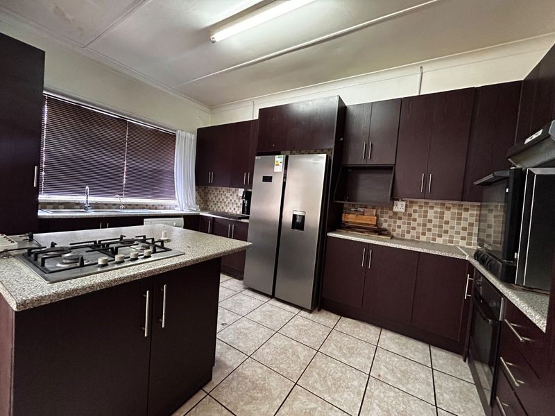 A functional kitchen featuring dark wood cabinetry, granite countertops, a gas hob, built-in oven, and tiled flooring with a mosaic backsplash.