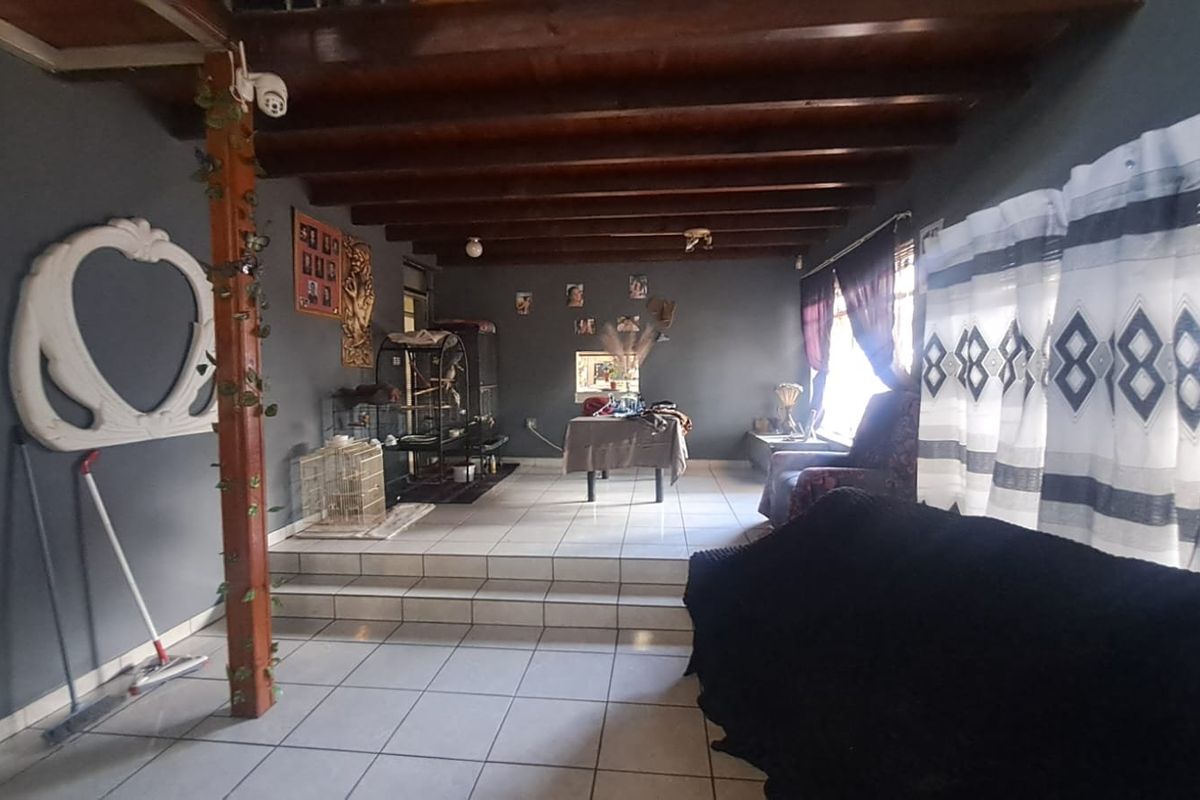 Spacious living area featuring exposed timber ceiling beams, tiled flooring, and a raised floor section, offering a versatile layout for family living.