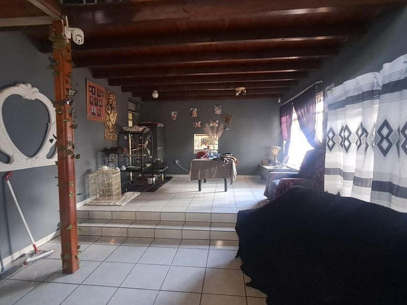 Spacious living area featuring exposed timber ceiling beams, tiled flooring, and a raised floor section, offering a versatile layout for family living.