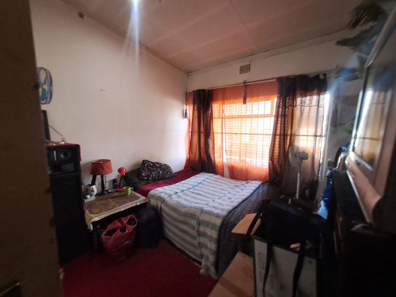 A bedroom featuring a large window with natural light, requiring cosmetic updates to the wall finishes and general maintenance.