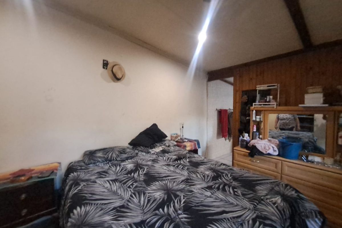 A bedroom featuring exposed timber ceiling beams and wood wall paneling, requiring cosmetic updates to improve the overall aesthetic and finish.
