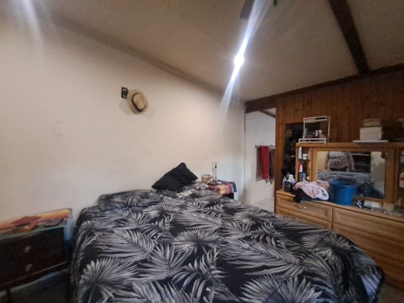 A bedroom featuring exposed timber ceiling beams and wood wall paneling, requiring cosmetic updates to improve the overall aesthetic and finish.