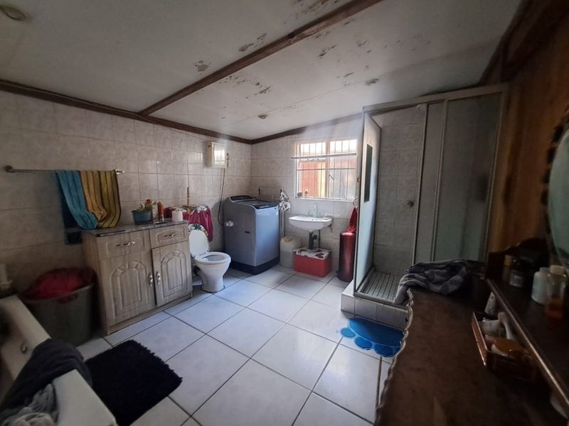 A functional bathroom featuring a shower enclosure, vanity cabinet, and basin, currently showing signs of ceiling wear and requiring cosmetic updates.