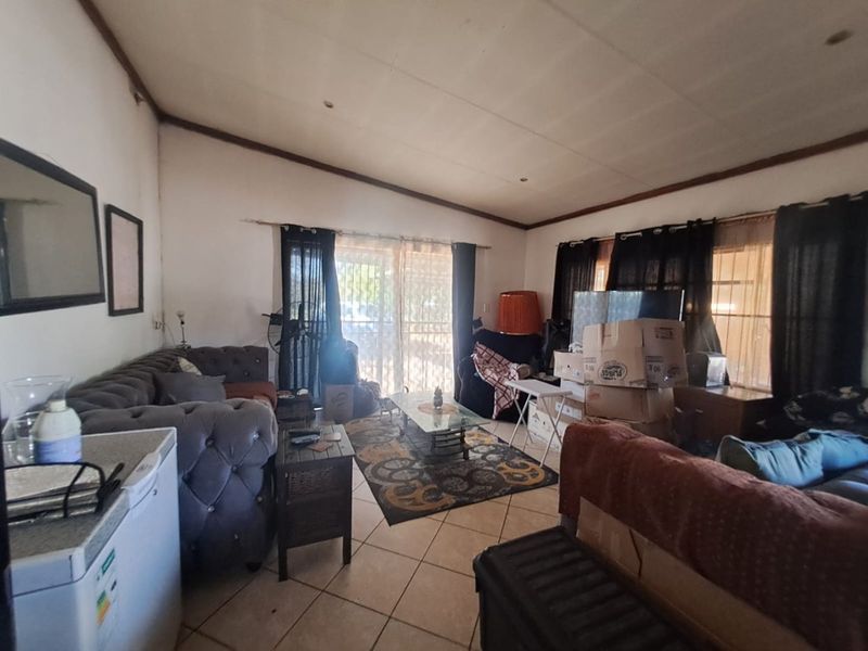 A living room featuring tiled flooring and a sliding glass door with security gate, requiring cosmetic updates to the ceiling and walls.
