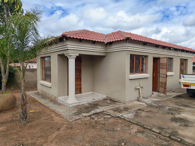 A single-story residential house featuring a tiled roof, concrete column entrance, and security gates, with a surrounding concrete apron and exterior wall finishes.