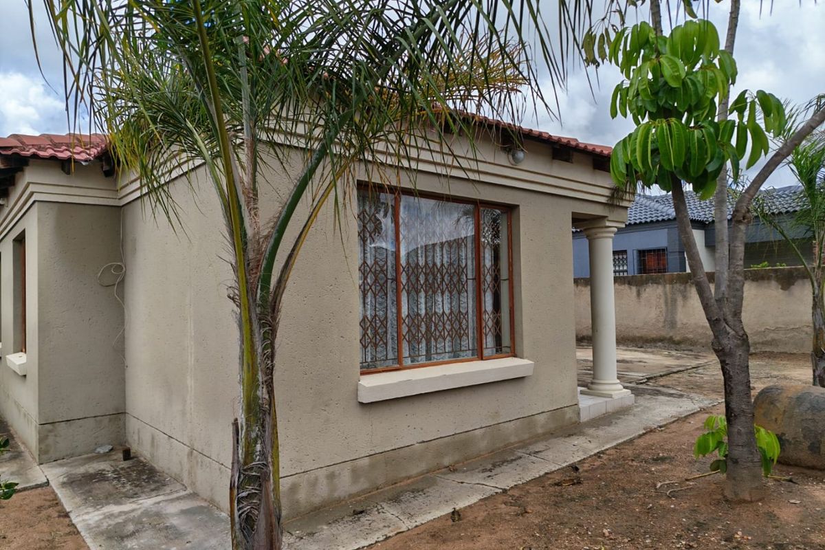 Rear exterior view of the house featuring plastered walls, a tiled roof, and a covered patio area with a concrete column.