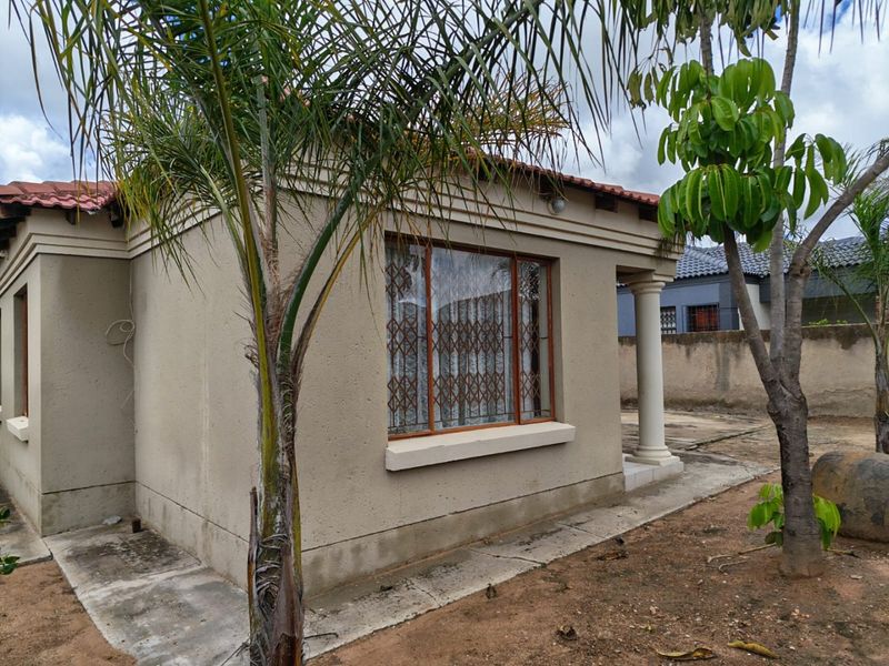 Rear exterior view of the house featuring plastered walls, a tiled roof, and a covered patio area with a concrete column.