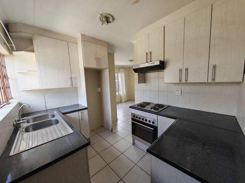 A functional kitchen featuring built-in cabinetry, a double basin sink, and an integrated electric stove with an extractor fan.