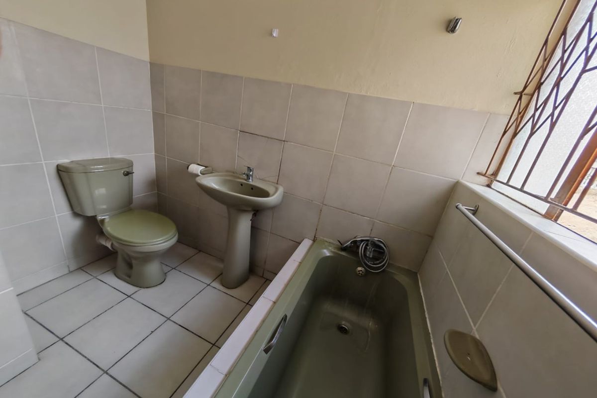 A functional bathroom featuring a bathtub, pedestal basin, and toilet with neutral wall and floor tiling.