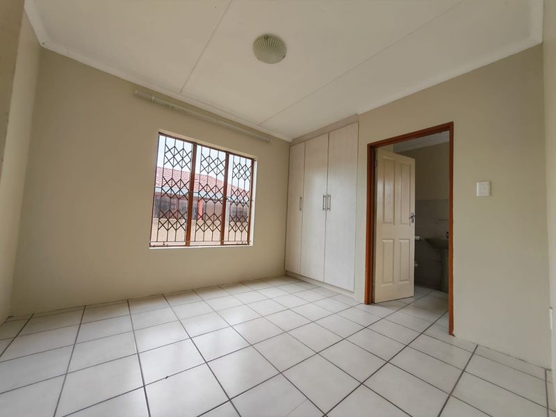 A clean, empty bedroom featuring tiled flooring, built-in cupboards, and a window with a security gate, offering a neutral space ready for personalization.