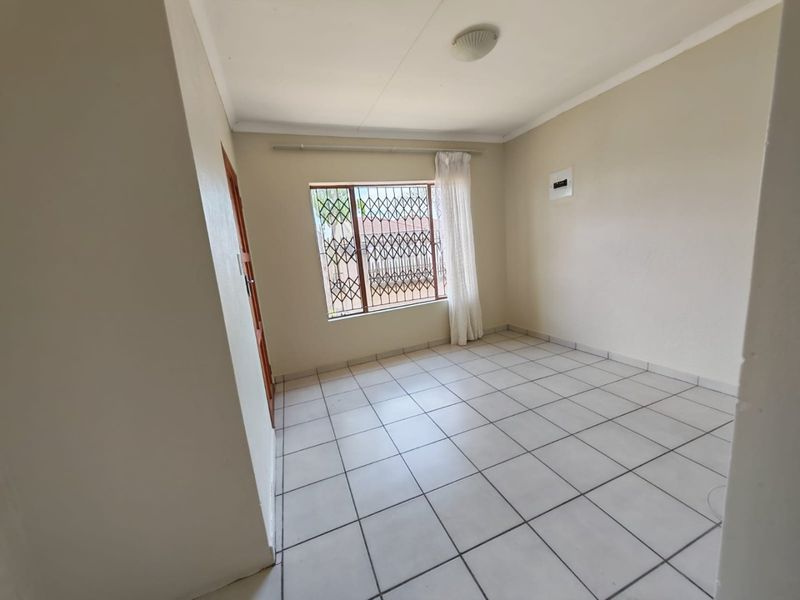 A clean, empty bedroom featuring neutral tiled flooring, a window with security bars, and a standard electrical distribution board.