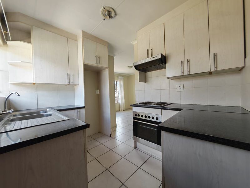 A functional kitchen featuring built-in cabinetry, dark laminate countertops, a stainless steel sink, and integrated oven with extractor fan, finished with tiled flooring.