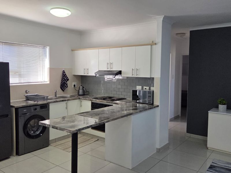 Modern open-plan kitchen featuring white cabinetry, marble-look countertops, integrated appliances, and a breakfast bar, seamlessly flowing into the living area.