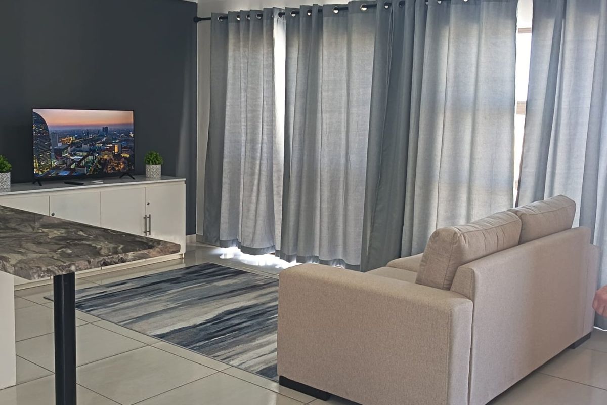 A well-maintained living room featuring neutral tiled flooring, a dark accent wall, and large windows dressed with floor-to-ceiling curtains.