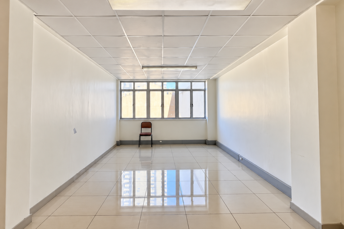 A bright, vacant office space featuring polished tiled flooring, a suspended ceiling with integrated lighting, and large windows providing natural light.