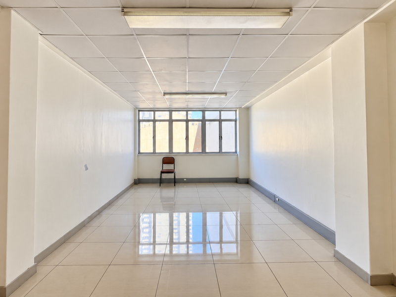 A bright, vacant office space featuring polished tiled flooring, a suspended ceiling with integrated lighting, and large windows providing natural light.
