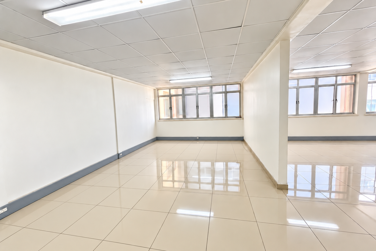 A bright, open-plan commercial office space featuring polished tiled flooring, suspended ceilings with integrated lighting, and large windows providing ample natural light.