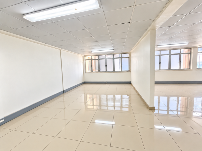 A bright, open-plan commercial office space featuring polished tiled flooring, suspended ceilings with integrated lighting, and large windows providing ample natural light.