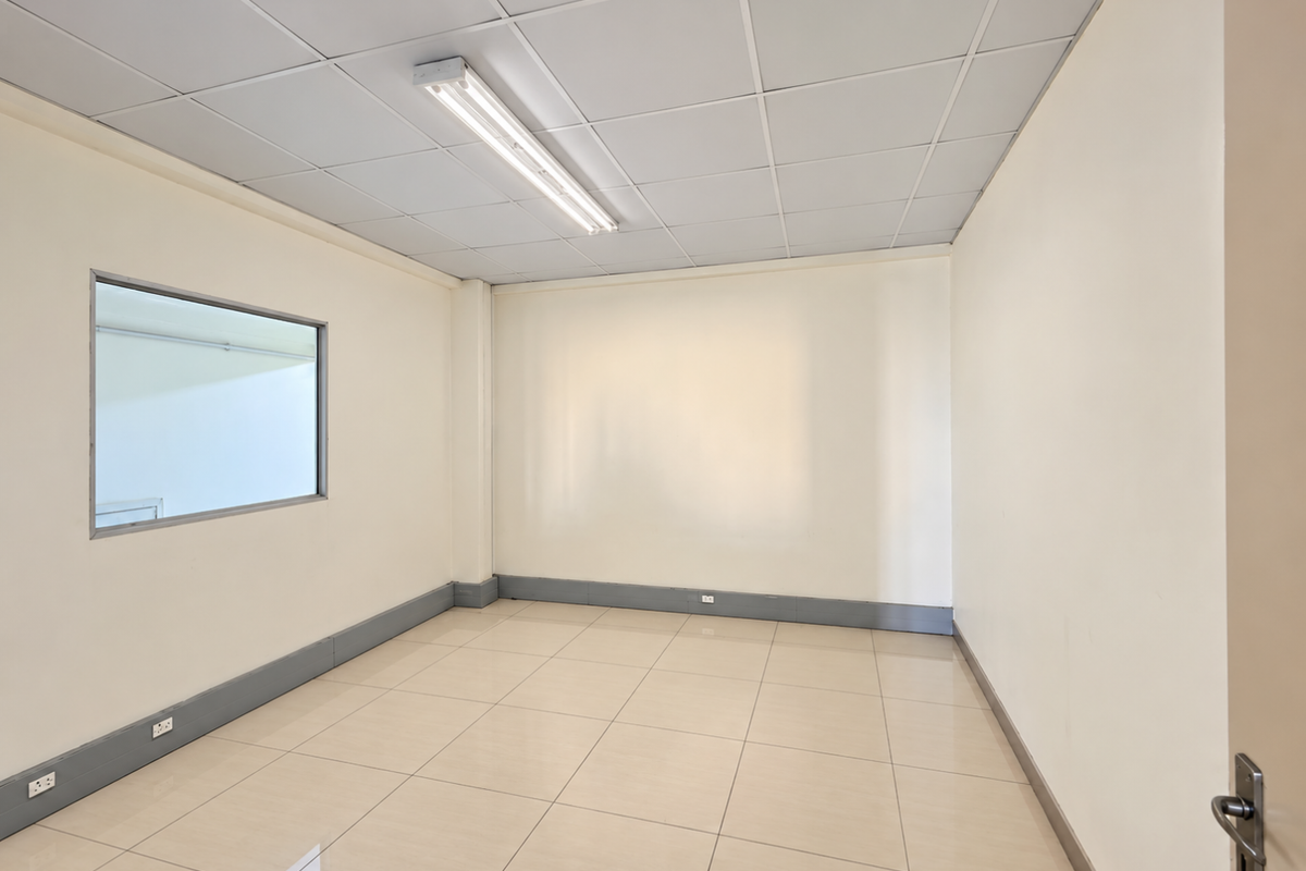 A clean, empty office space featuring tiled flooring, a suspended ceiling with integrated lighting, and an internal window providing natural light.