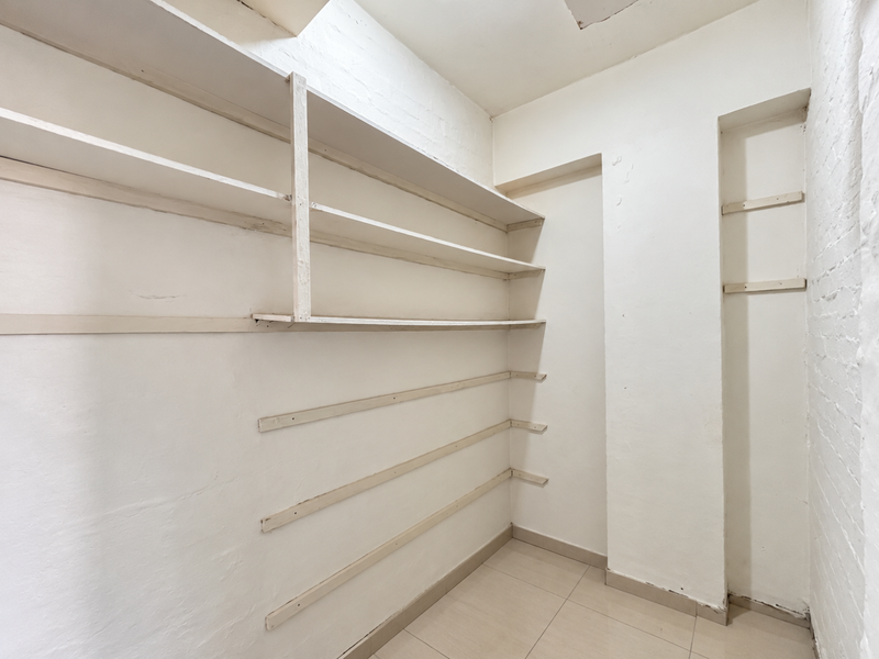 A vacant utility or storage room featuring built-in wall shelving and tiled flooring, requiring minor cosmetic repairs to the walls and ceiling.