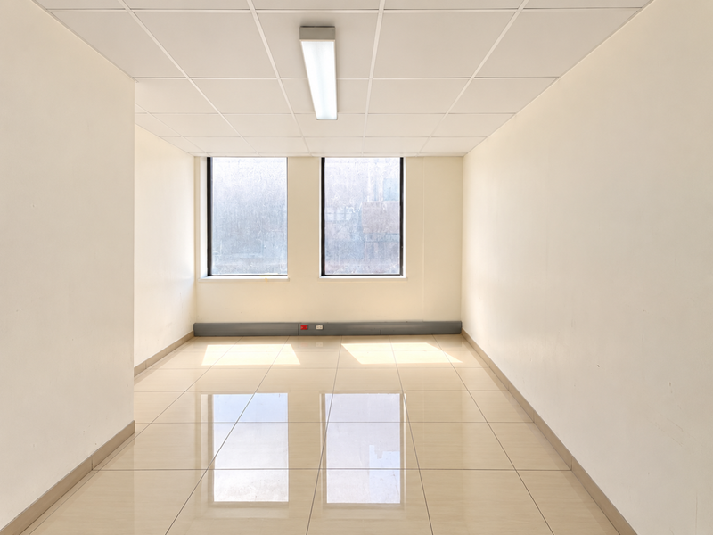 A bright, empty office space featuring tiled flooring, a suspended ceiling with integrated lighting, and large windows providing natural light.