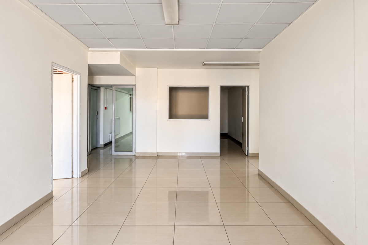 A bright, vacant commercial office space featuring neutral ceramic tile flooring, a suspended ceiling with integrated lighting, and multiple internal access points.