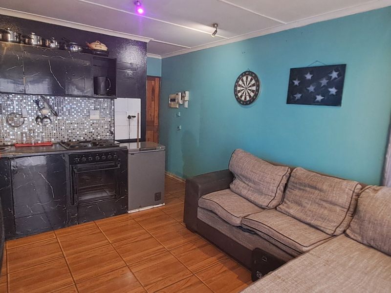 Open-plan living area featuring a compact kitchen with built-in oven, gas hob, and mosaic tile backsplash, finished with tiled flooring throughout.