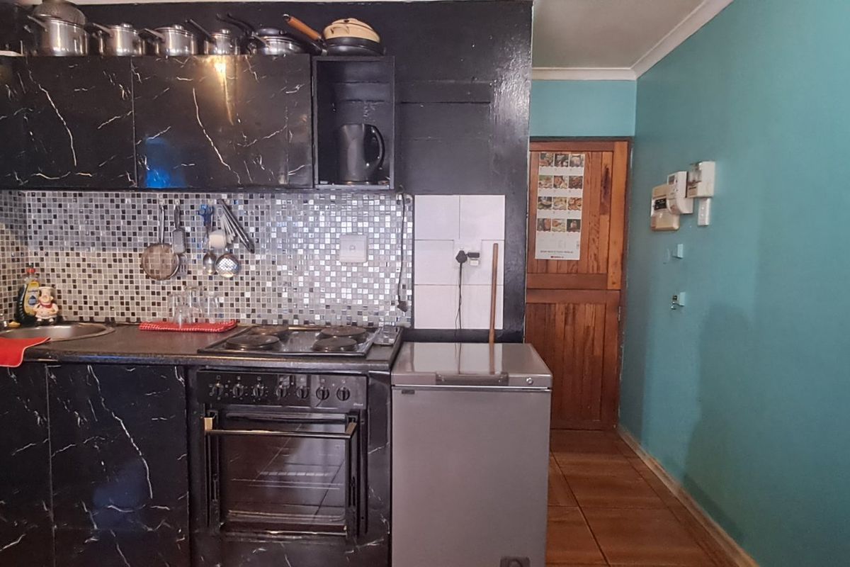 Compact kitchen featuring black marble-effect cabinetry, mosaic tile backsplash, built-in oven and hob, and tiled flooring.