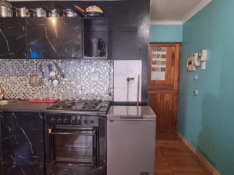Compact kitchen featuring black marble-effect cabinetry, mosaic tile backsplash, built-in oven and hob, and tiled flooring.