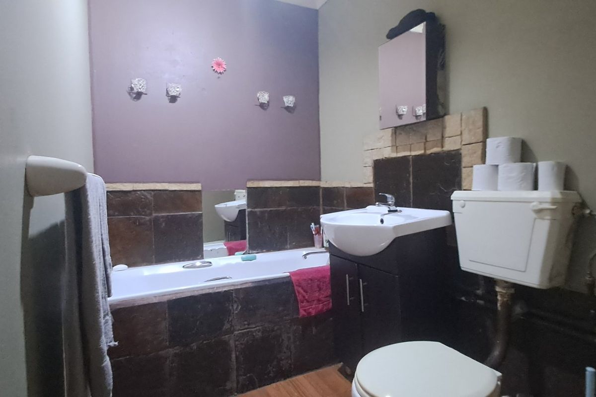 A functional bathroom featuring a bathtub, vanity unit with basin, and toilet, with dark tiled splashbacks and visible plumbing fixtures.