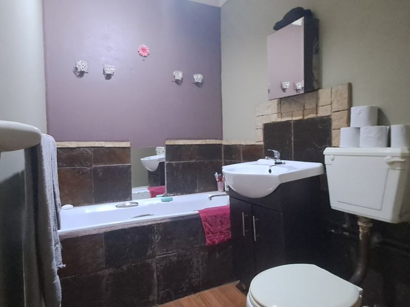 A functional bathroom featuring a bathtub, vanity unit with basin, and toilet, with dark tiled splashbacks and visible plumbing fixtures.