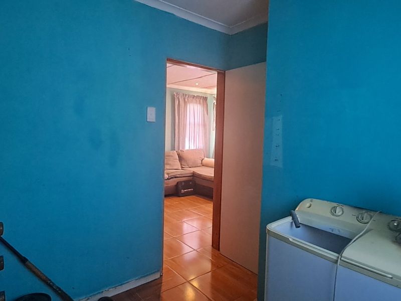 A laundry area featuring blue painted walls and a doorway leading to an adjacent living space with tiled flooring.