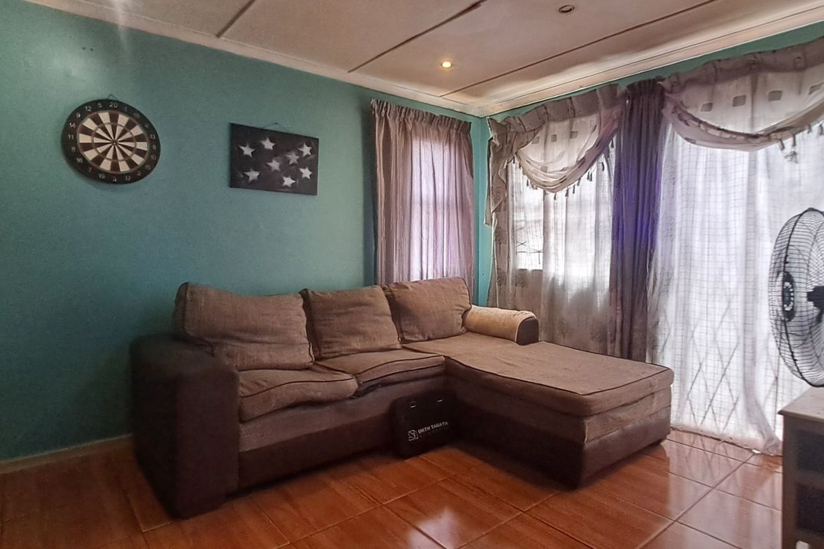 A living room area featuring tiled flooring and a sliding glass door providing natural light, with potential for cosmetic updates to finishes.