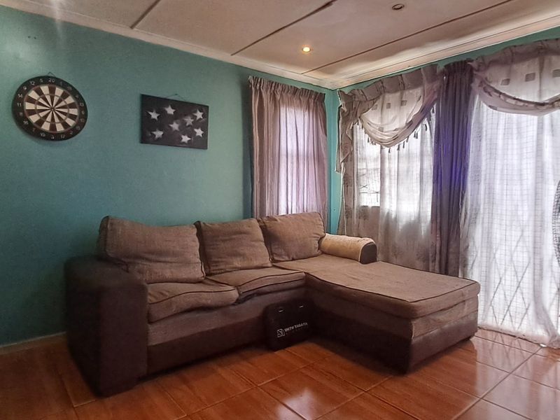 A living room area featuring tiled flooring and a sliding glass door providing natural light, with potential for cosmetic updates to finishes.