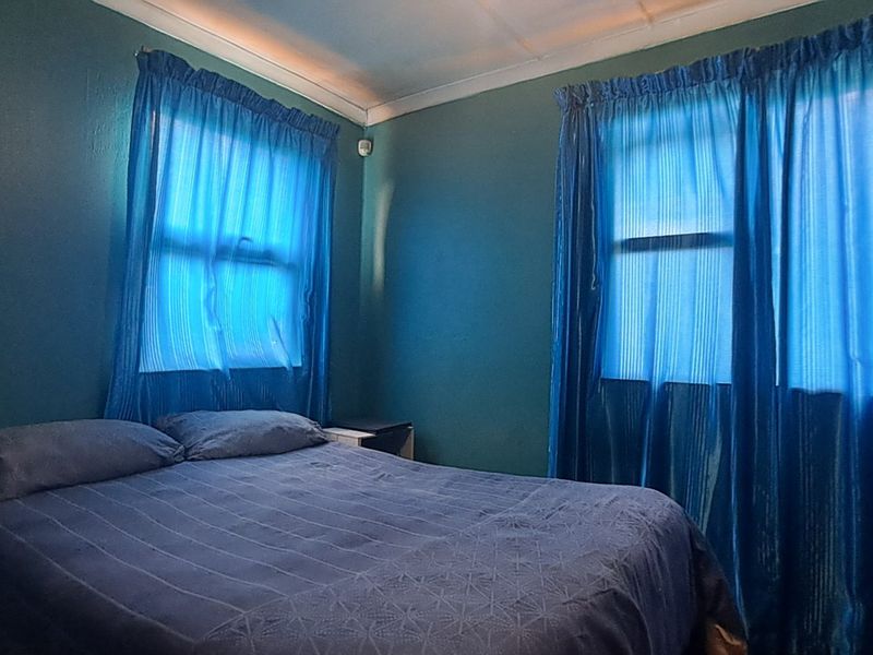 A bedroom featuring dark painted walls and dual windows with blue curtains, requiring cosmetic updates to improve the overall aesthetic and finish.