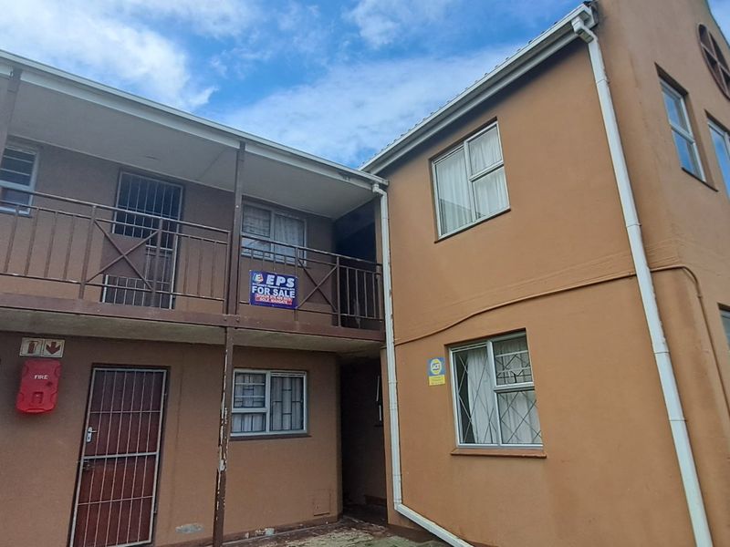 Exterior view of an apartment building featuring metal security gates, balcony railings, and an external staircase, showing signs of weathering and maintenance needs.
