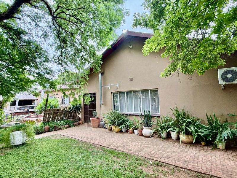 Rear exterior view of the house featuring a brick paved patio area, established garden, and wall-mounted air conditioning unit.