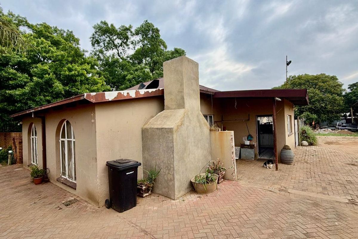 Rear view of the property featuring a brick chimney, paved driveway, and covered patio area with arched window detailing.